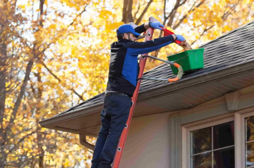 Worker cleaning gutters from a ladder.