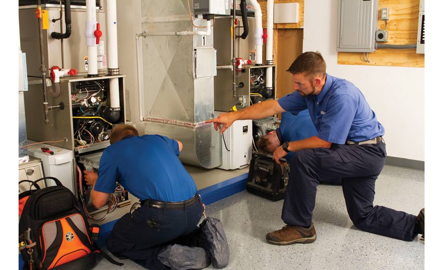 Two technicians work on a furnace system in a utility room.