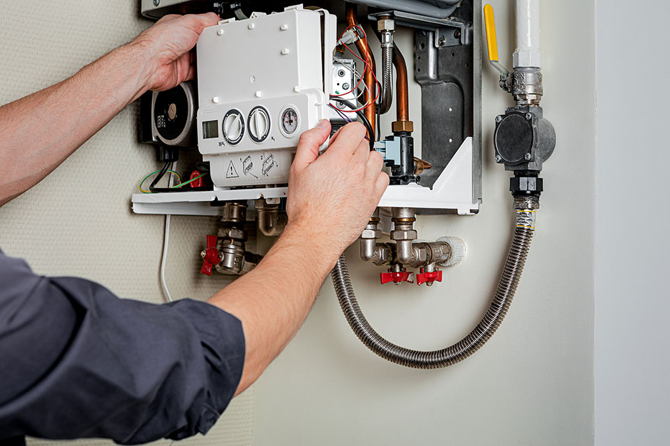 An HVAC technician adjusts the control panel on an open wall-mounted boiler unit.
