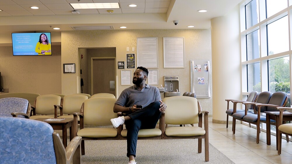 Man sitting in a medical waiting room with empty chairs around him.